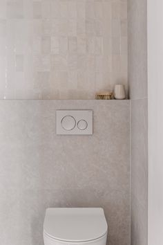 a white toilet sitting in a bathroom next to a wall mounted faucet and tiled walls