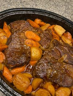 a pot roast with carrots and gravy in a black bowl on a counter