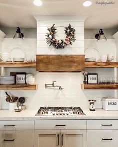 a white kitchen with open shelves and wreath on the wall above the stove top,