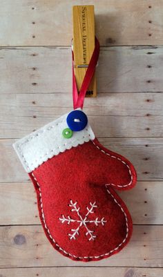 an oven mitt ornament hanging on a wooden wall with a red ribbon