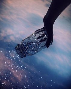 a hand holding a glass jar in the sky with stars on it and water droplets all around