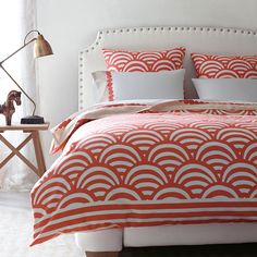 a bed with an orange and white comforter on top of it next to a lamp