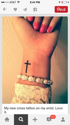 a woman's wrist with a cross tattoo on it and pearls around the wrist