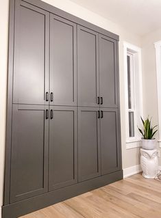 a large gray cabinet sitting in the corner of a room next to a window and potted plant