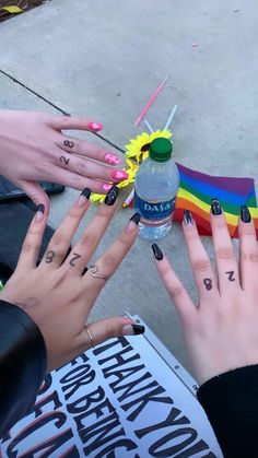 two women with black fingernails and tattoos on their fingers, one holding a water bottle while the other holds a rainbow flag