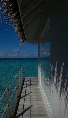 a view of the ocean from a wooden deck on an over - water villa with thatched roof