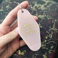 a person holding a white plastic keychain with the words witch by nature written on it