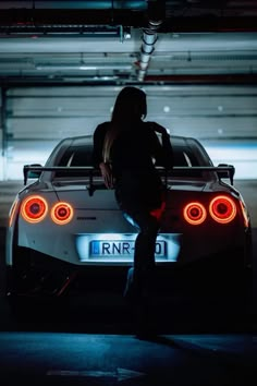 a woman standing next to a white sports car in a parking garage with the lights on