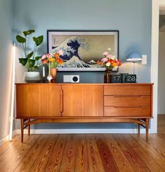 a living room with wooden floors and a large painting on the wall above it's entertainment center