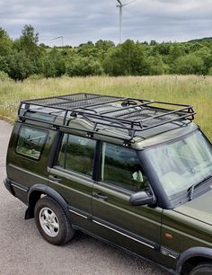 a green land rover is parked on the side of the road in front of a wind turbine