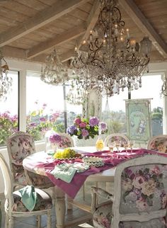 a dining room with chandelier and flowers on the table in front of large windows