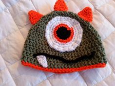 a crocheted hat with an eyeball on the front and bottom, sitting on top of a bed