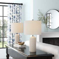 two lamps are sitting on a table in front of a mirror and window with blue curtains