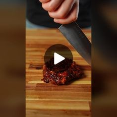 a person cutting up food on top of a wooden cutting board with a large knife