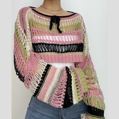 a woman wearing a pink and black sweater with tassels on her shoulders, standing in front of a white wall