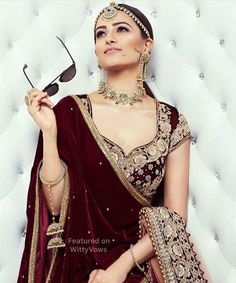 a woman in a red and gold bridal outfit holding up a pair of scissors