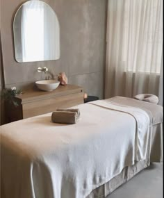 a white bed sitting next to a wooden dresser under a round mirror on top of a wall