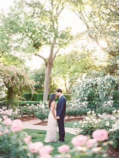 a bride and groom standing in the middle of a garden with pink flowers on it