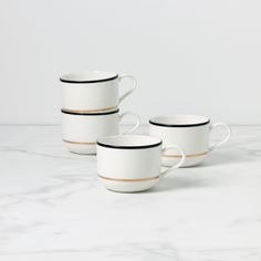 three white coffee cups with black rims on a marble countertop in front of a white wall