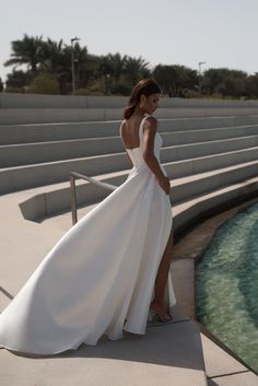 a woman in a white dress is standing on steps near the water and looking at something