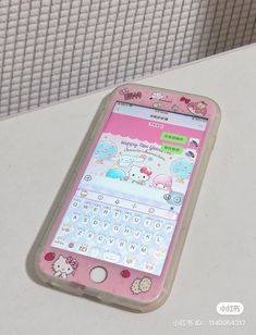 a pink cell phone sitting on top of a white table next to a wall with hello kitty stickers