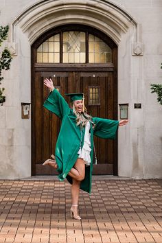 a woman in a graduation gown and cap is dancing on the brick floor outside an old building