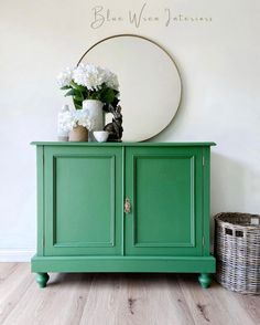 a green cabinet with flowers on top and a round mirror above it