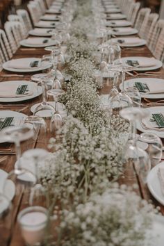 a long wooden table with white plates and place settings on it, along with baby's breath flowers