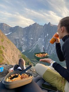 a woman sitting on top of a mountain drinking from a bottle and eating food out of a bowl