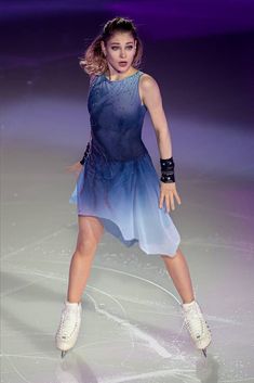 a female figure skating on the ice in a blue dress and black gloves with her arms outstretched