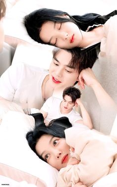 three people laying in bed with white sheets on top of them and one person holding the other