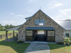 a stone barn with a metal roof and two garages on the side of it