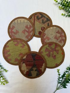 four embroidered coasters sitting on top of a table next to some green leaves and flowers