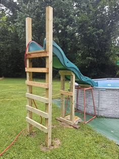 a wooden structure with a slide in the back ground and a swimming pool behind it