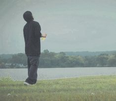 a man standing on top of a lush green field next to a lake holding a yellow frisbee