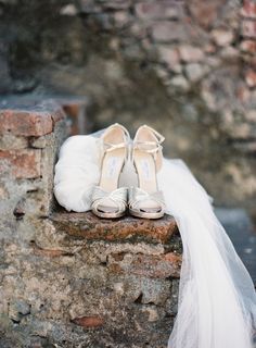 two pairs of wedding shoes sitting on top of a stone wall next to a veil