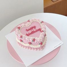 a pink heart shaped cake sitting on top of a white table next to a card