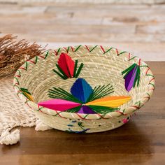 a woven basket with tassels on top of a wooden table next to a potted plant