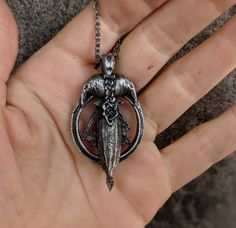 a hand holding a silver pendant with an angel on it's back and wings in the middle