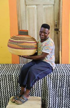 a man sitting on top of a bed holding a basket over his head and smiling