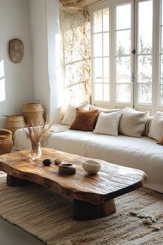 a living room with white couches and wooden table in front of large open windows