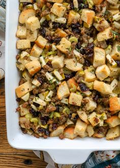 a white casserole dish filled with stuffing and cranberries on a wooden table