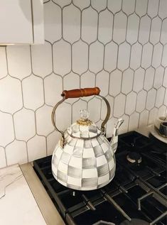 a tea kettle sitting on top of a stove in front of a white tiled wall