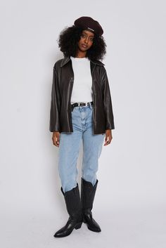 a woman in black leather jacket and jeans with cowboy boots standing against a white background