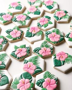 decorated cookies with pink flowers and green leaves on a white tablecloth covered in icing