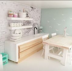 a small kitchen with white walls and wooden table in the center, along with shelving on the wall