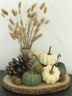 some white and green pumpkins are sitting on a wooden plate with pineconies