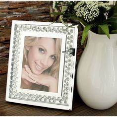 a white vase with some flowers in it and a picture frame on the table next to it