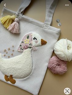 a white tote bag with a ducky embroidered on it and two balls of yarn next to it