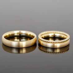 two gold wedding rings sitting on top of a black table next to eachother